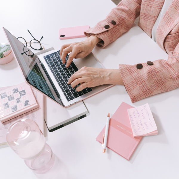 Freelance Marketing Managerin I Anne Meinhardt Dekoratives Bild zur Leistung Freelance Marketing Management von Marketing-Expertin Anne Meinhardt aus Dresden. Zu sehen ist eine Frau im rosa Blazer arbeitet am Laptop im Homeoffice, umgeben von Notizbüchern, Smartphone und Arbeitsutensilien.